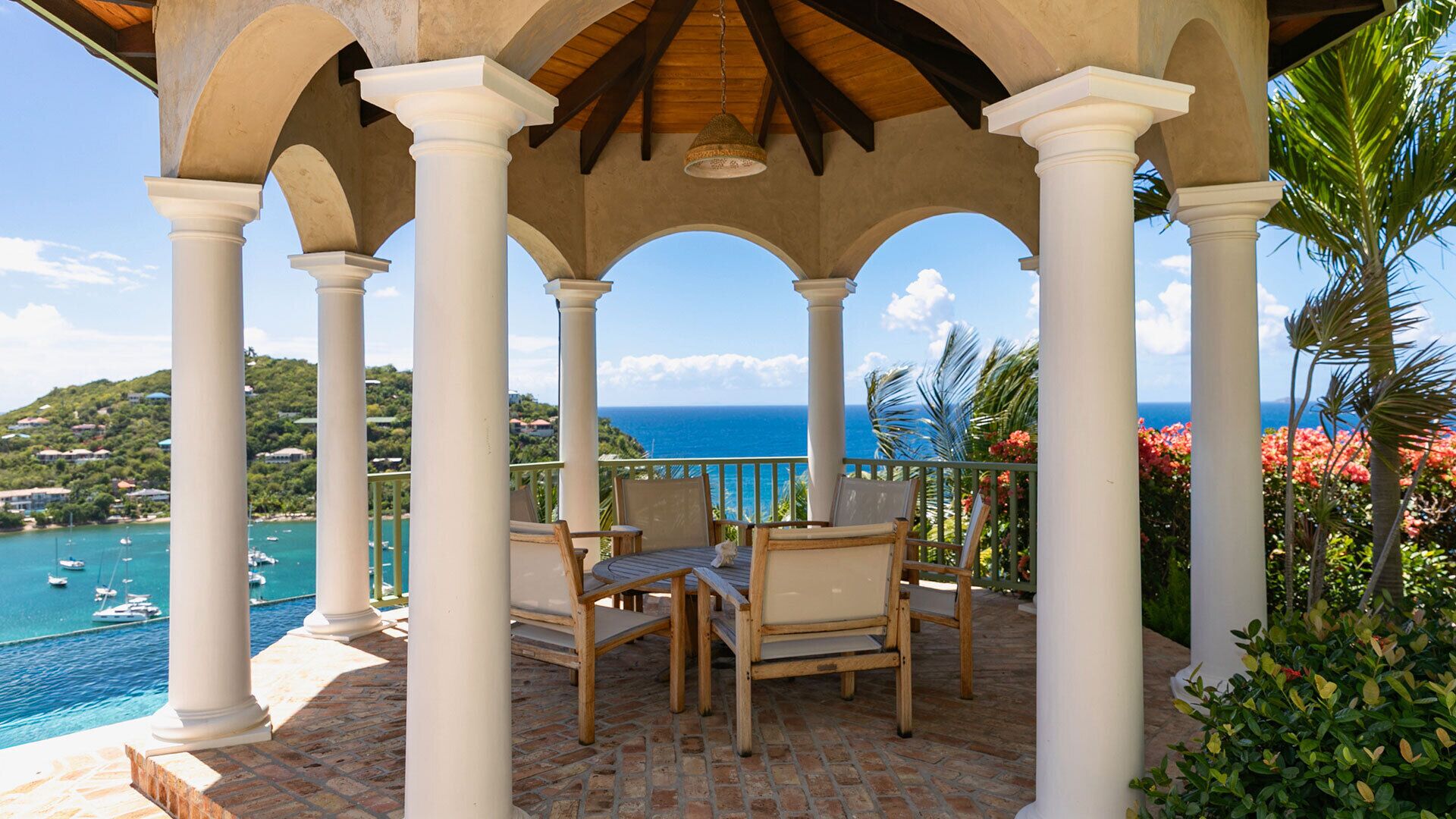 A covered outdoor seating area with a view of the sea and boats.