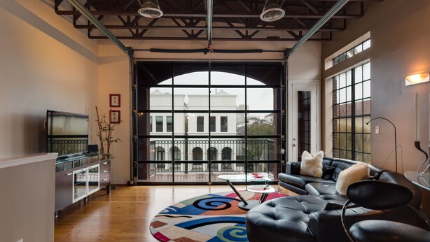A spacious living area with a large window, a black leather sofa, a glass coffee table, and a decorative rug. - Montrose NY Style Brick Home with a chef kitchen! (Houston)