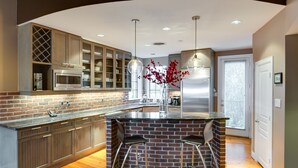 A modern kitchen with a brick backsplash, stainless steel appliances, and a central island with bar stools. - Montrose NY Style Brick Home with a chef kitchen! (Houston)