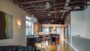 A spacious living area with a leather sofa, dining table, and chairs, a kitchen in the background, and a high ceiling with exposed beams. - Montrose NY Style Brick Home with a chef kitchen! (Houston)