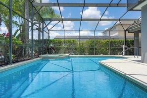 Une piscine d’un bleu éclatant, protégée par une paroi en verre, entourée de plantes tropicales et encadrée par une structure métallique.
