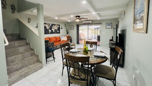 A dining area with a table set for four, a sofa, a staircase, and a ceiling fan.