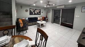 A modern living room with a sofa, dining table, and chairs. There is a world map on the wall, a ceiling fan, and a sliding glass door.