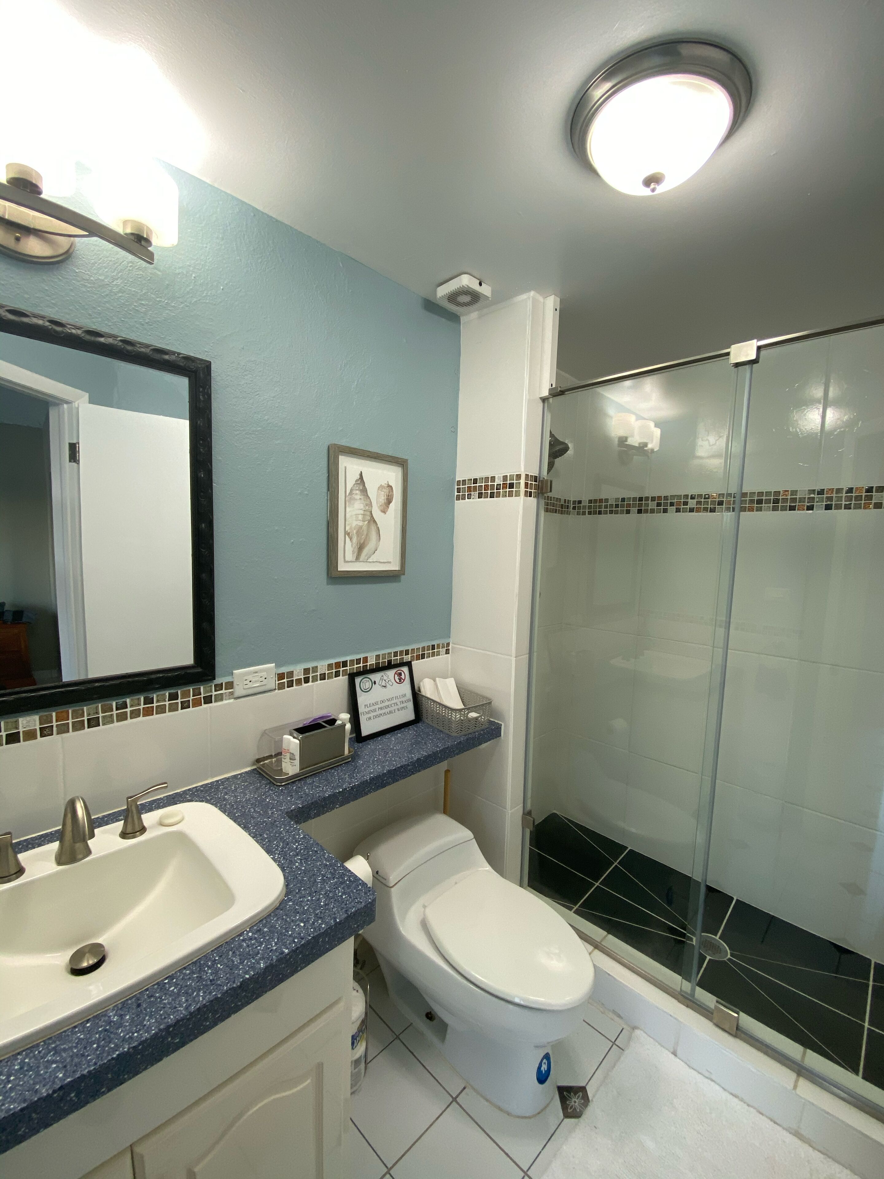 Une salle de bain avec deux lavabos, des toilettes, une douche avec une porte en verre et un miroir avec un cadre.