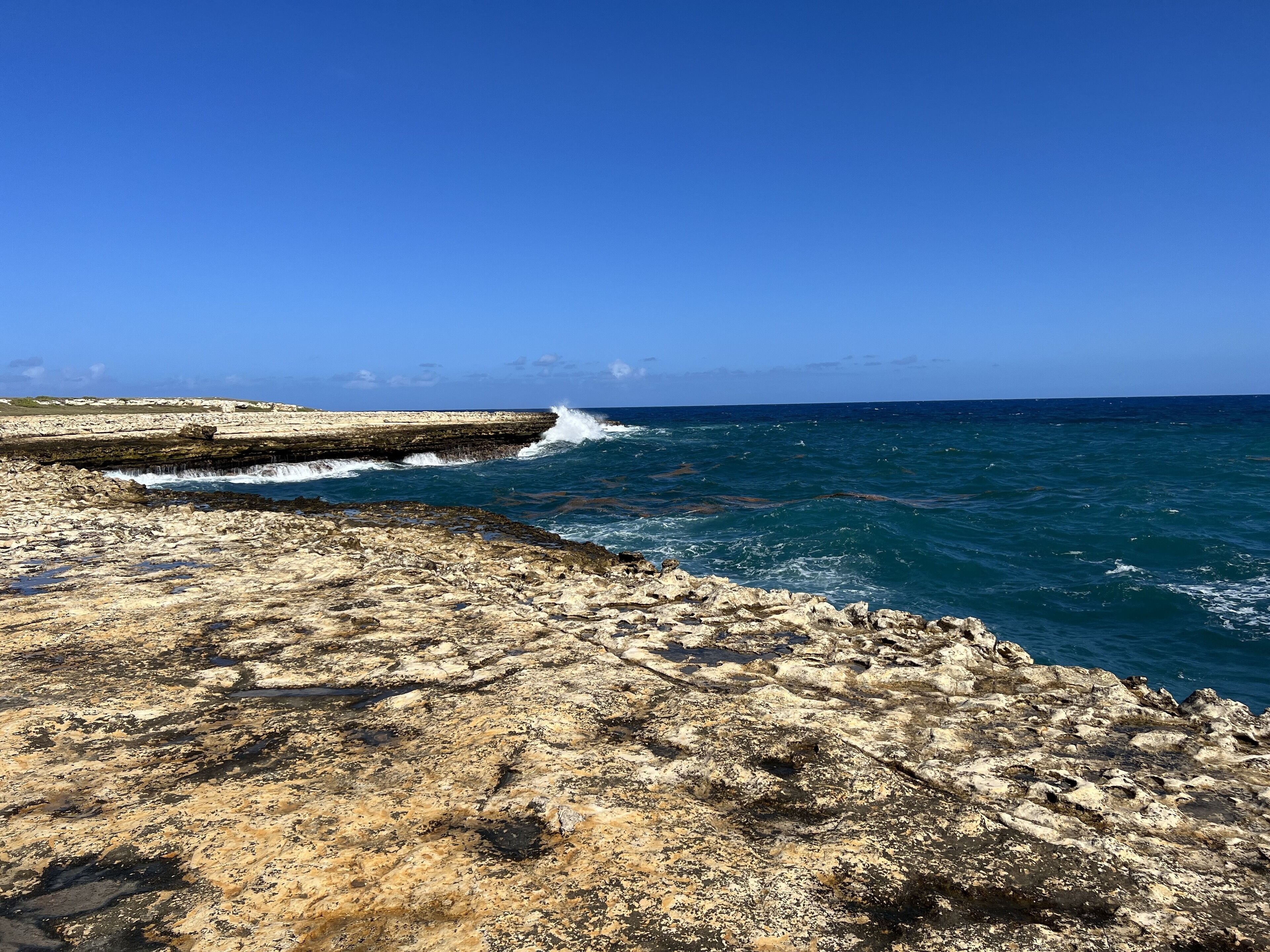 A rocky coastline with waves crashing against a low sea wall.
