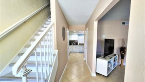 Ein geräumiger Flur mit einer Treppe zu einer zweiten Etage, ein Küchenbereich mit weißen Schränken und ein Essbereich mit Fernseher und Zierpflanzen.