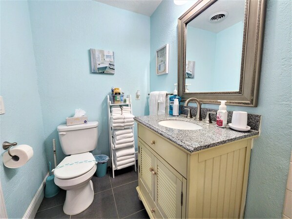 A bathroom with a toilet, sink, and mirror. There are towels and toiletries on the sink counter.