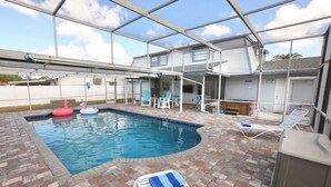 Ein überdachter Pool im Freien mit einer Ziegelterrasse, Liegestühlen und Schwimmspielzeug.