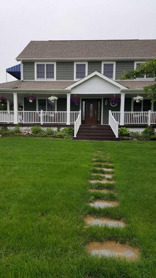A two-story house with a front porch, a staircase leading to the entrance, and a well-maintained lawn. - Beautiful Colonial Mint Condition Summer House Walking Distance to Beach (Jamesport)