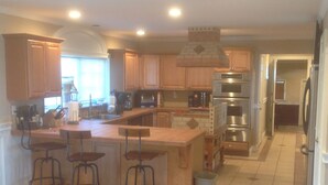 A spacious kitchen with wooden cabinets, a central island with bar stools, stainless steel appliances, and a tiled floor.