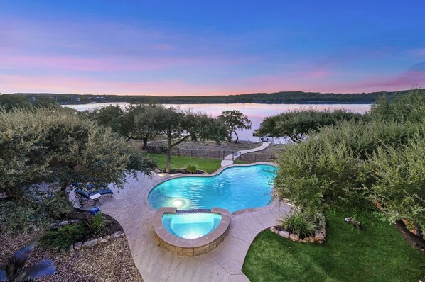 A swimming pool with a hot tub, surrounded by a landscaped garden and a view of a lake.