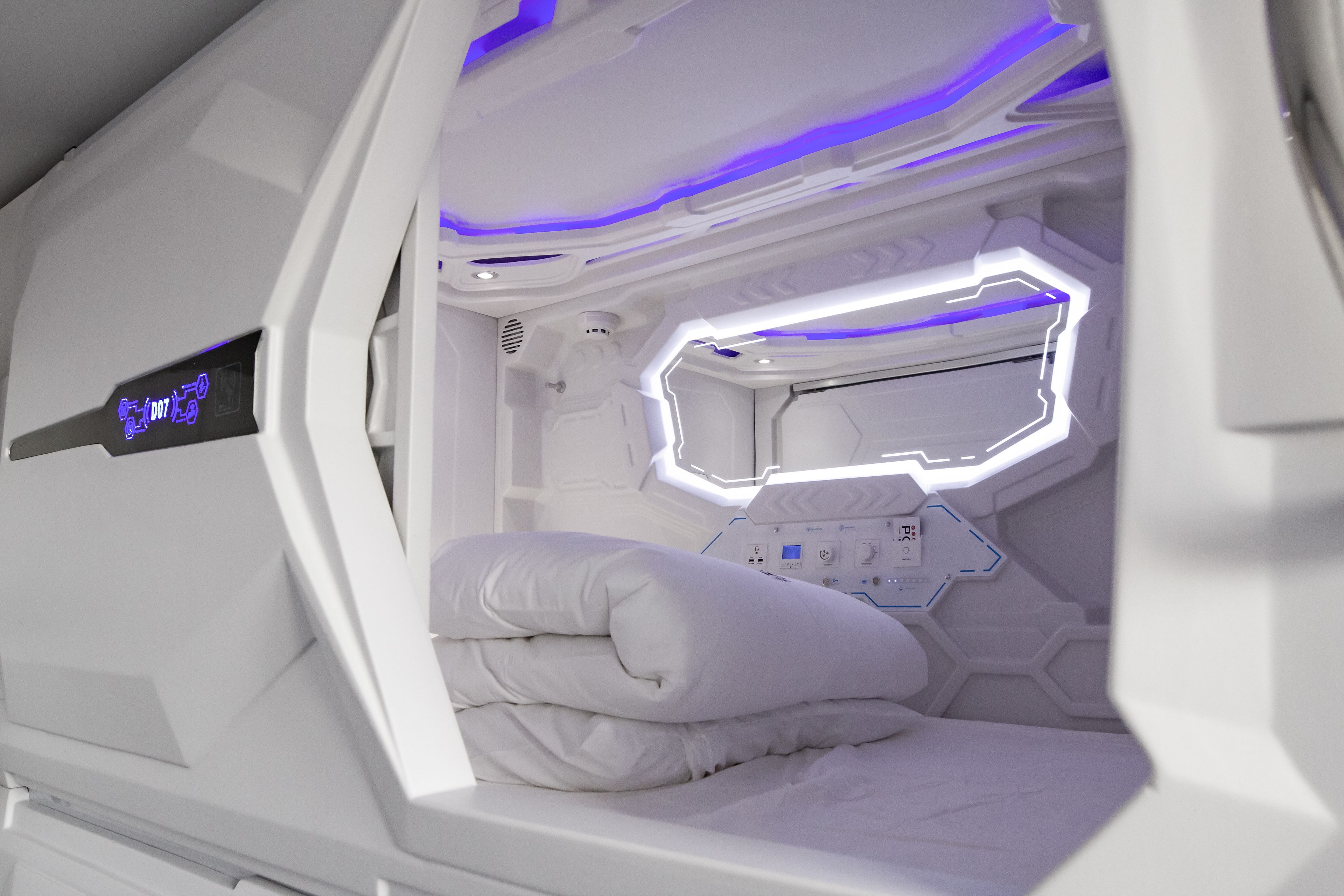 A futuristic room with a control panel, a bed, and a window.