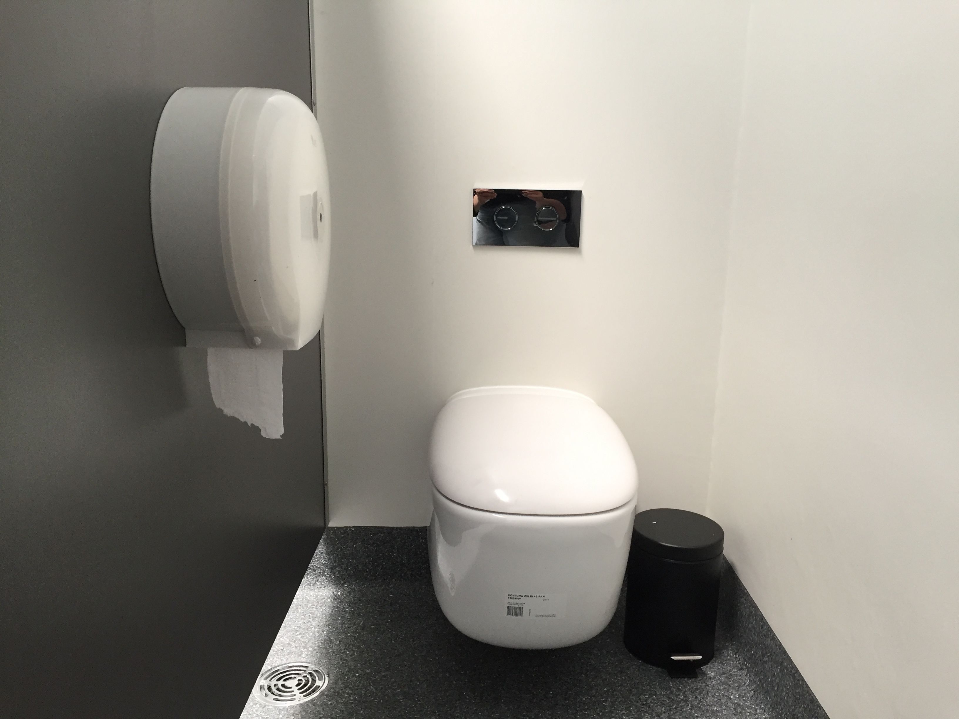 A modern bathroom with a toilet, a paper towel dispenser, and a trash bin.