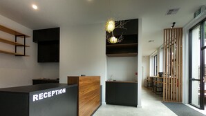 A reception area with a reception desk, wooden shelves, a modern chandelier, and a view of the outdoors through large windows. - Pod Inn (Launceston)