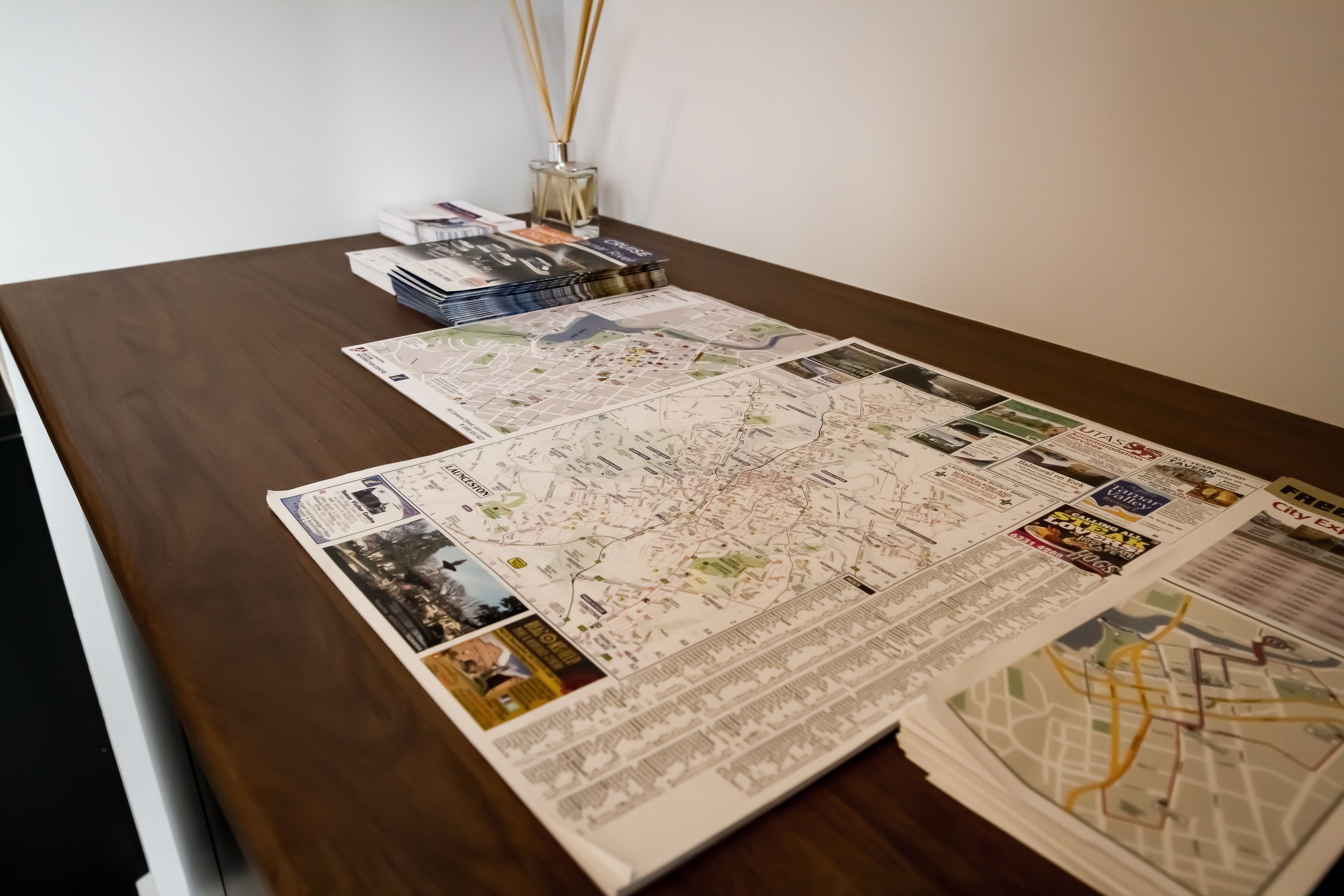 Una mesa de madera con dos mapas grandes, una pila de libros y un florero de vidrio con cañas.