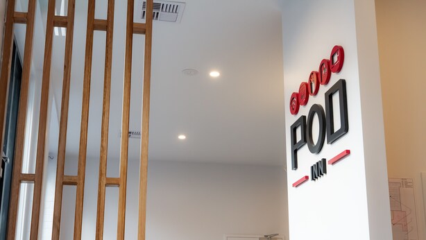 A room with a white wall, a wooden partition, and a door with a fire safety sign. - Pod Inn (Launceston)