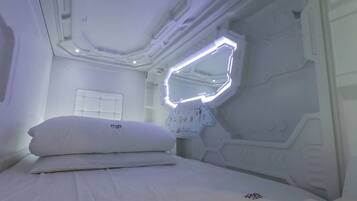 A modern, minimalist bedroom with a neatly made bed, a wall-mounted mirror, and a control panel.