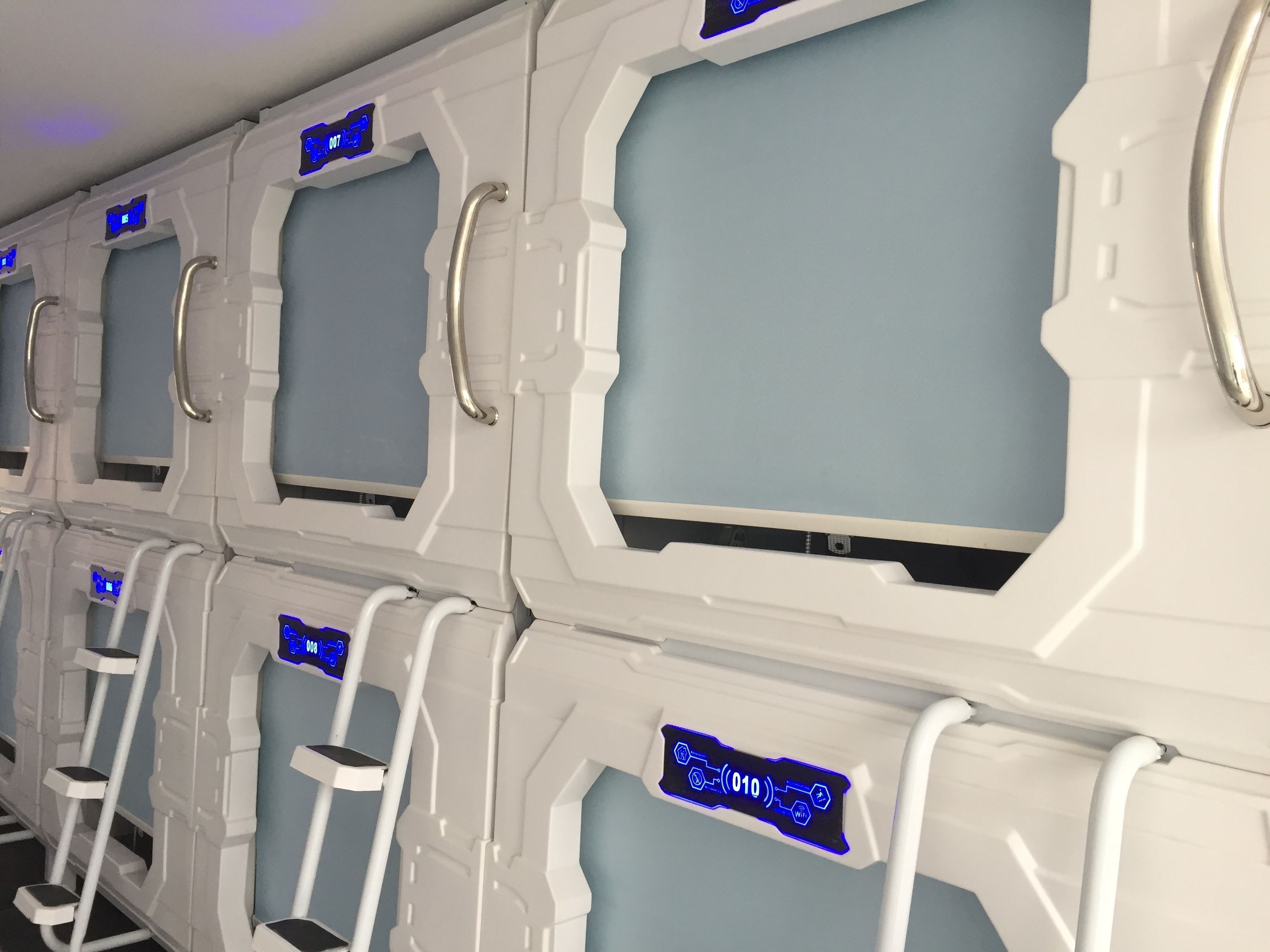 Een rij futuristische, witte, hightech pods met blauwe digitale schermen en metalen handgrepen.