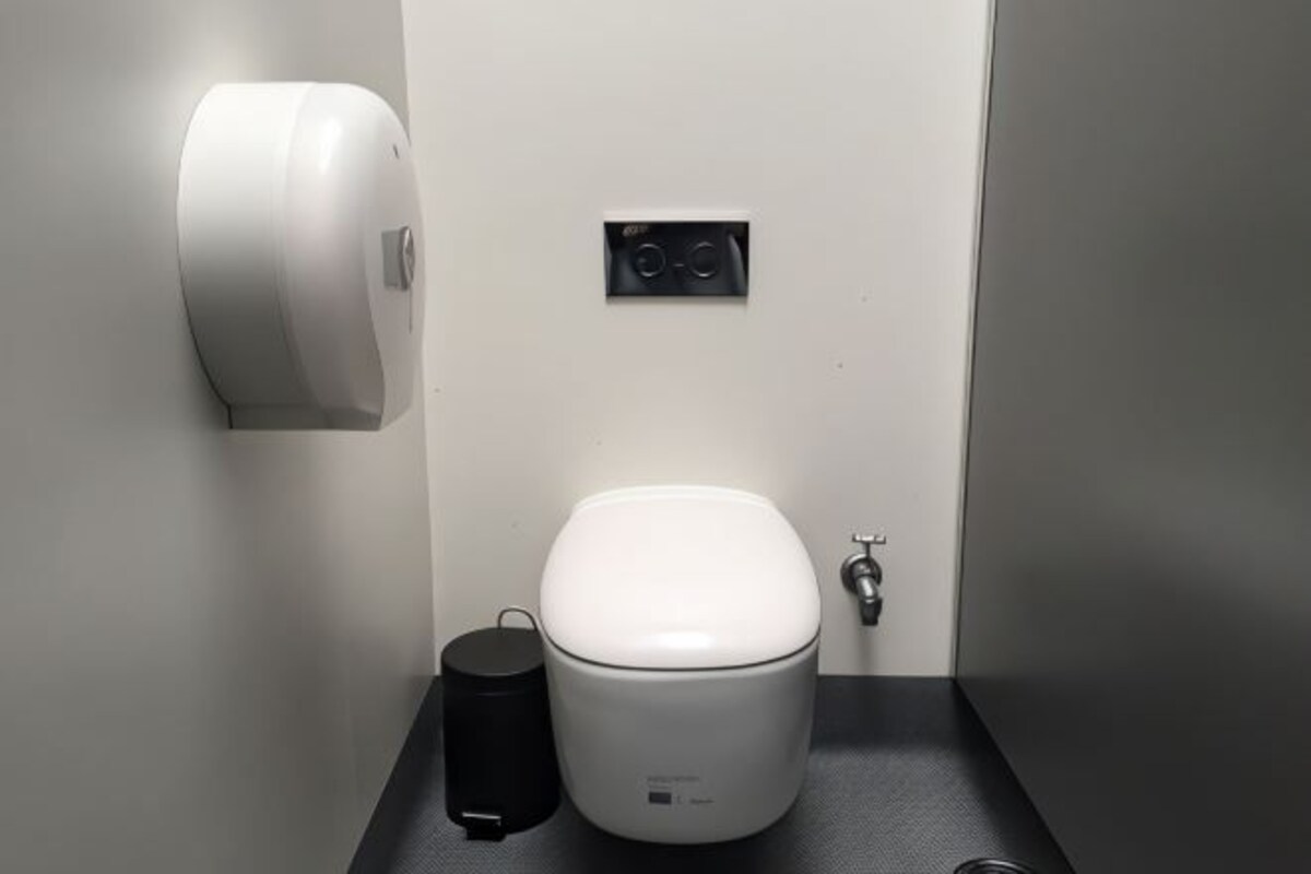 A compact, modern bathroom with a white toilet, a black trash bin, and a hand dryer mounted on the wall.