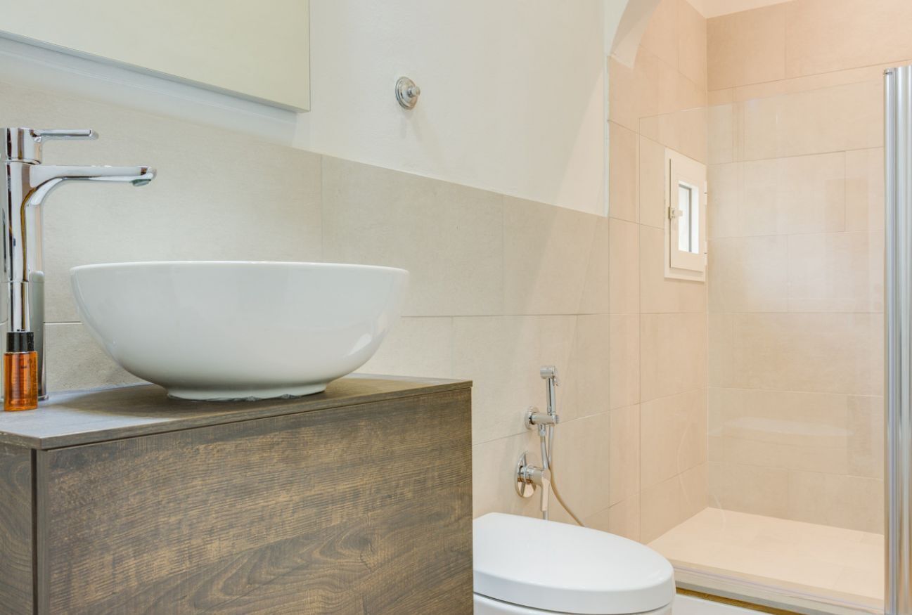A bathroom with a wooden vanity, a white sink with a large bowl, a toilet, and a glass shower enclosure.