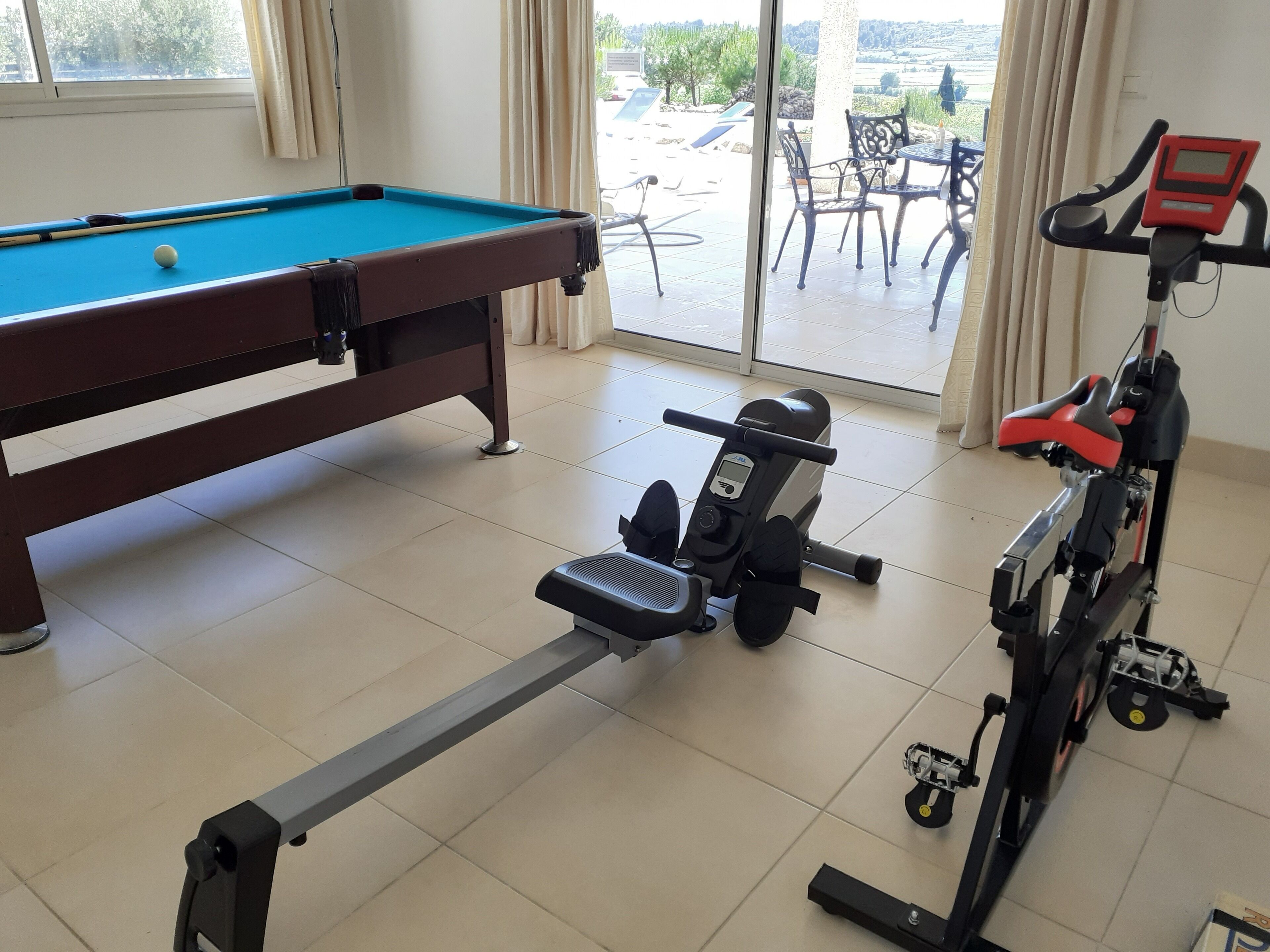 A room with a pool table, exercise equipment, and a view of the outdoors.