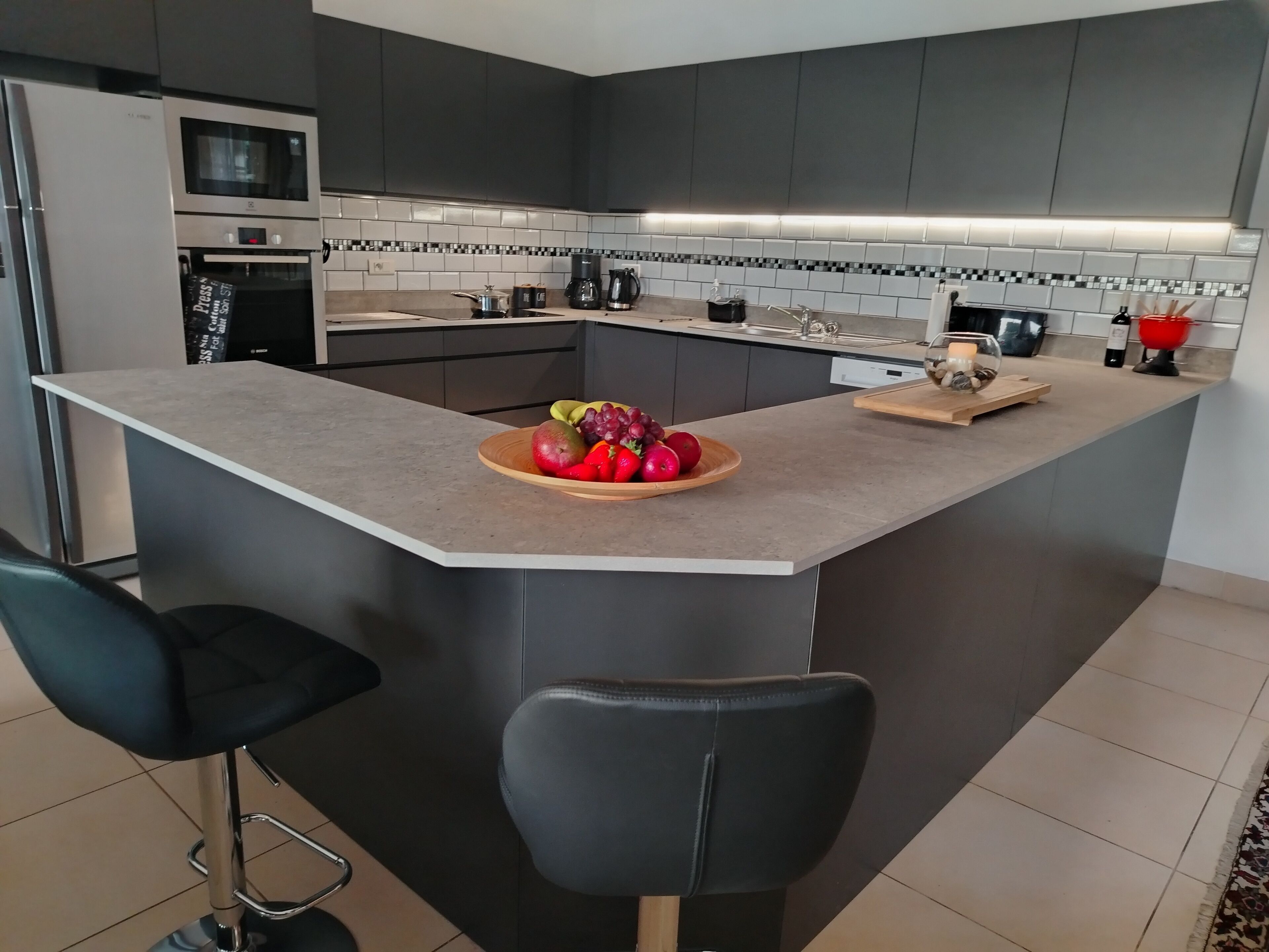 Een moderne keuken met een centraal eiland, barstoelen, een magnetron, oven en een koffiezetapparaat.