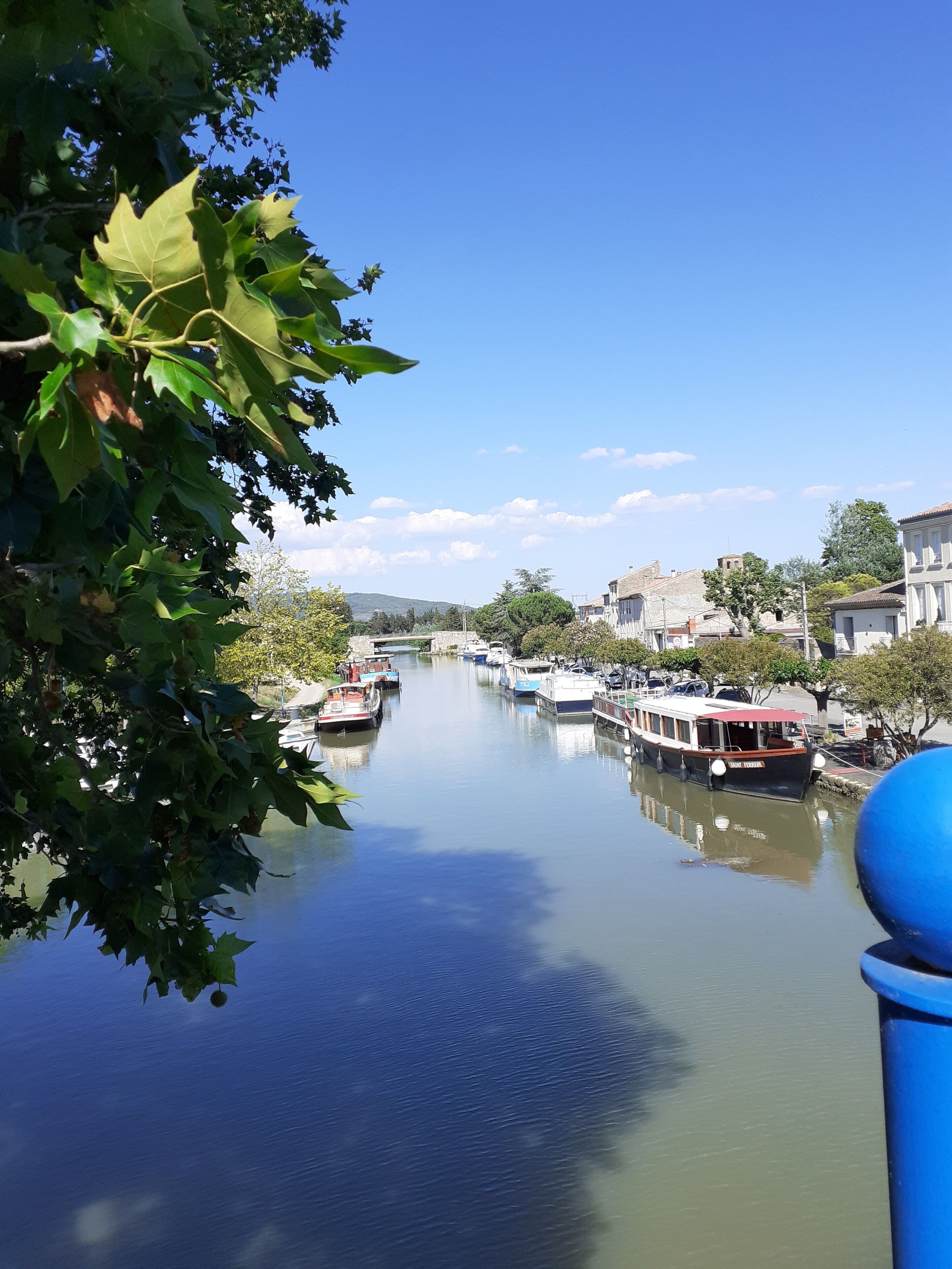Ein ruhiger Fluss mit vertäuten Booten am Ufer, umgeben von Gebäuden und Grünflächen.