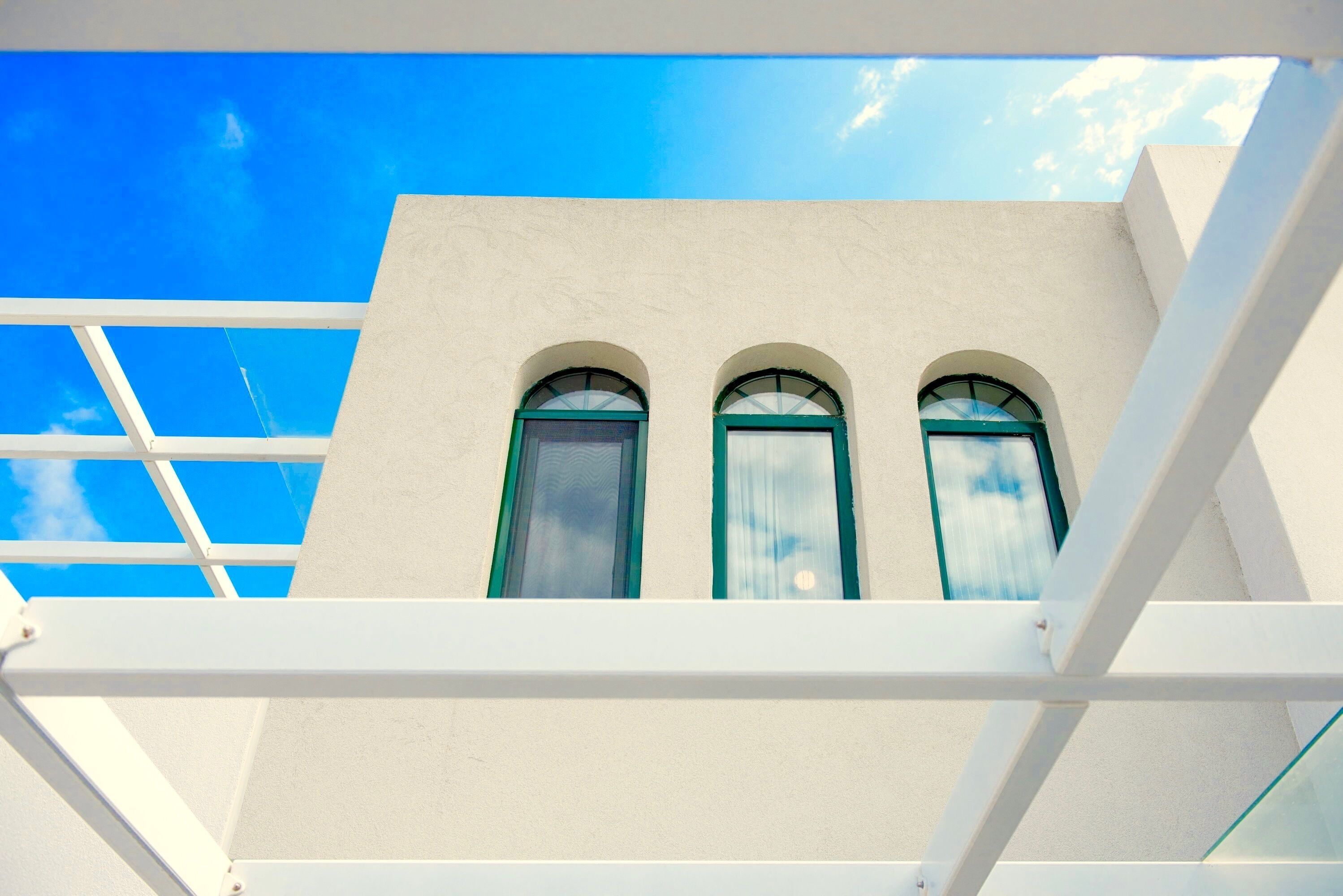 Fachada de edifício com três janelas em arco e céu azul claro.