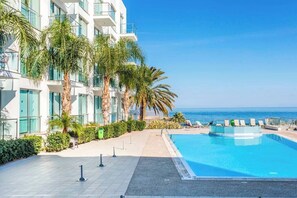 A modern hotel with a pool, palm trees, and a view of the ocean. - 1 Bedroom Apartment in the heart of Protaras within walking distance (Protaras)