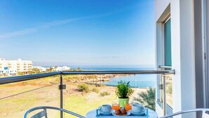 Ein Balkon mit gedecktem Tisch für das Frühstück, mit Blick auf die Küste und Gebäude in der Ferne.