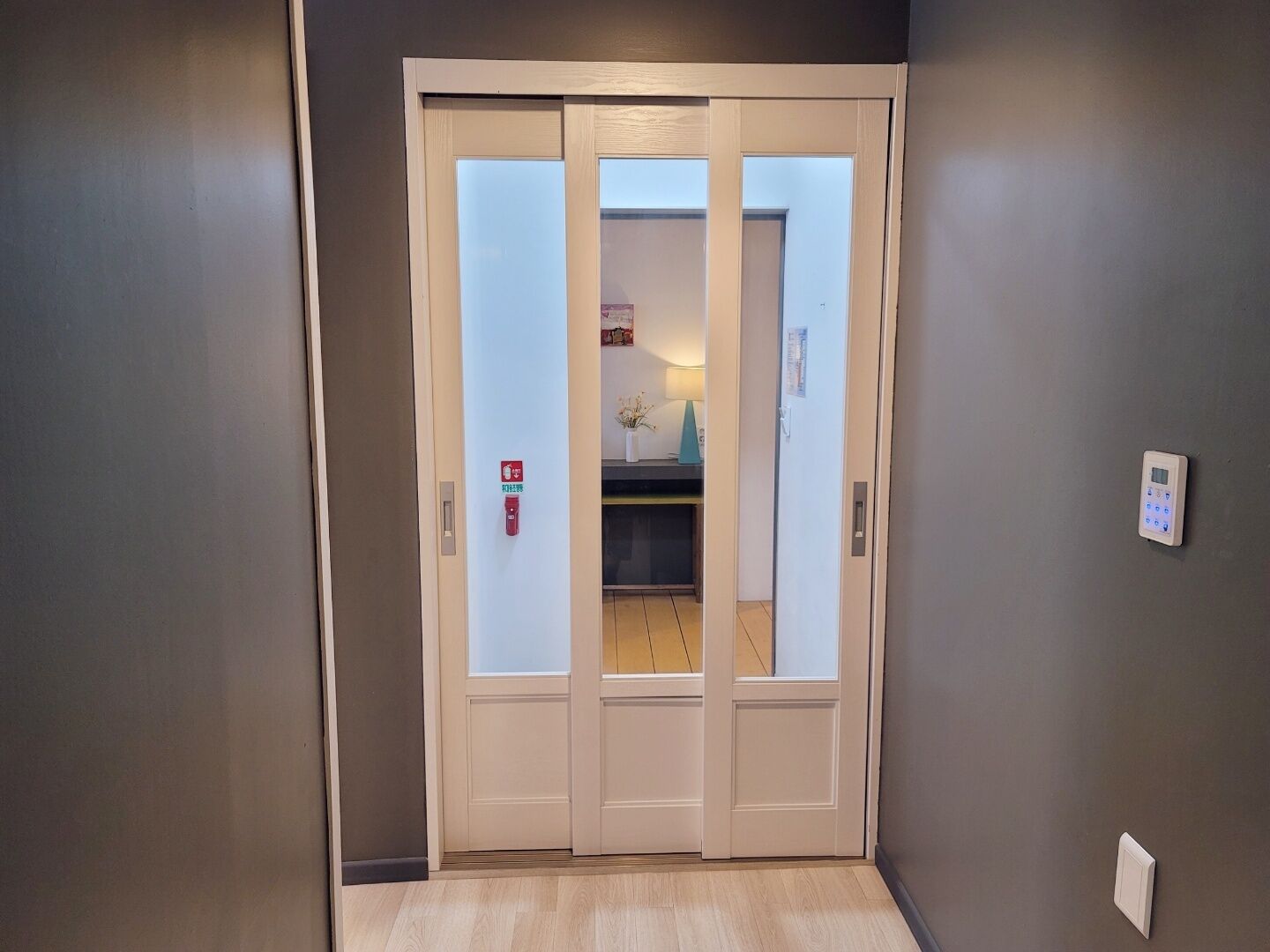 A closed door with frosted glass panels, a fire alarm, and a wall-mounted intercom system.