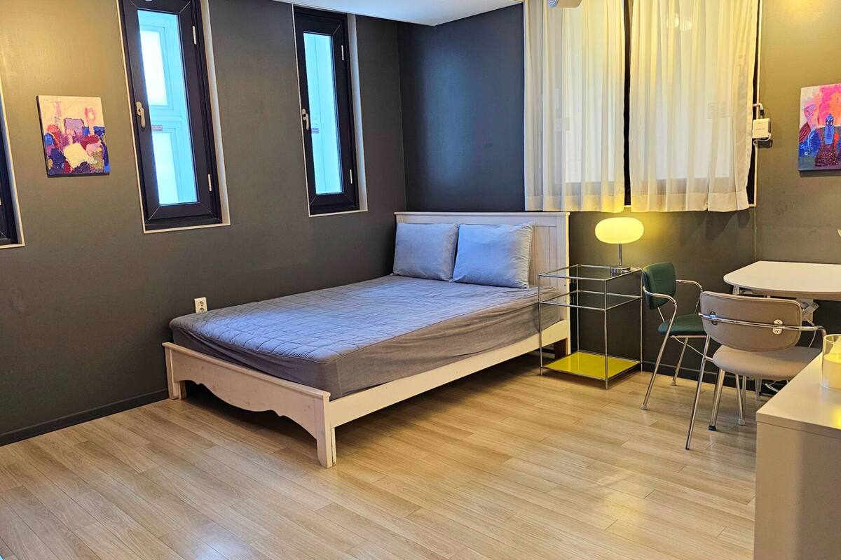 A modern bedroom with a bed, bedside table, chair, and a desk with a lamp.