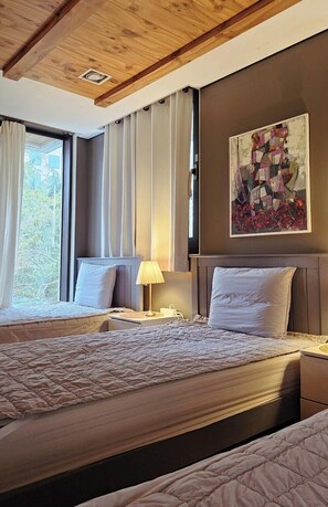 A hotel room with two beds, a wooden ceiling, a painting on the wall, and a window with curtains. - Gallery Family Hotel (Mokpo)