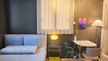Een slaapkamer met een bed, een bureau, twee stoelen, een lamp, een vaas met bloemen en een schilderij aan de muur.