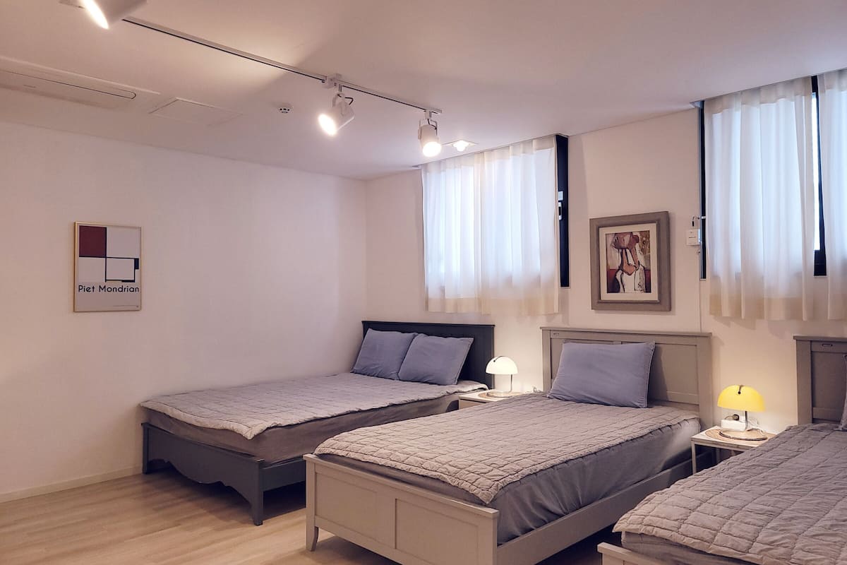 A modern bedroom with two beds, a ceiling light, a bedside table with a lamp, and a framed picture on the wall.