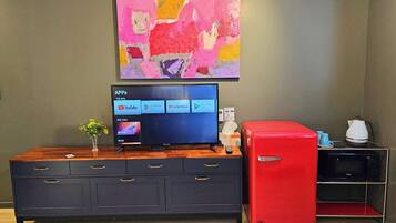 Una sala de estar moderna con un televisor de pantalla plana, un refrigerador rojo, un armario de madera y un cuadro abstracto colorido en la pared.
