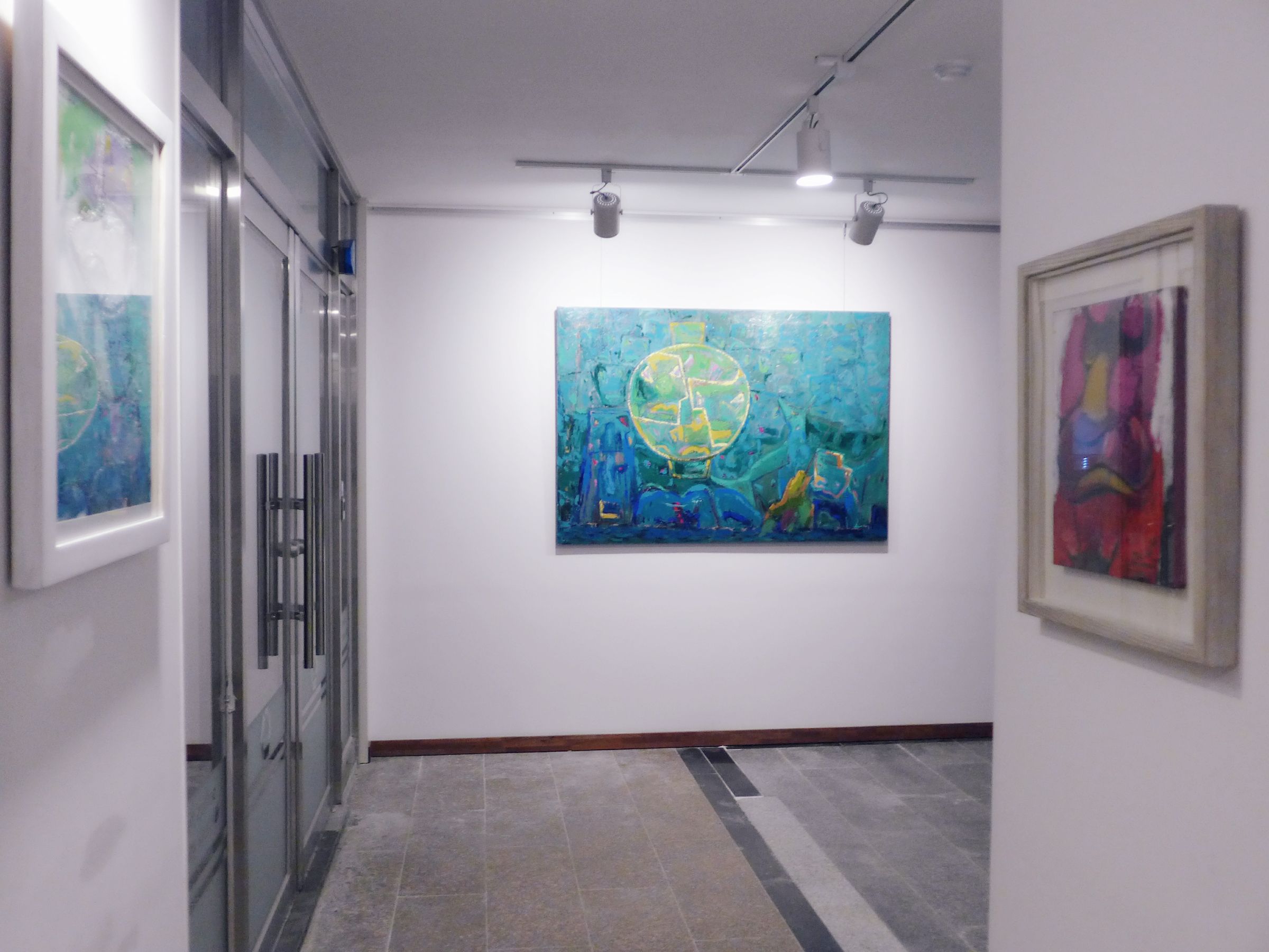 A hallway with a large abstract painting on the wall, a glass door on the left, and a framed picture on the right.