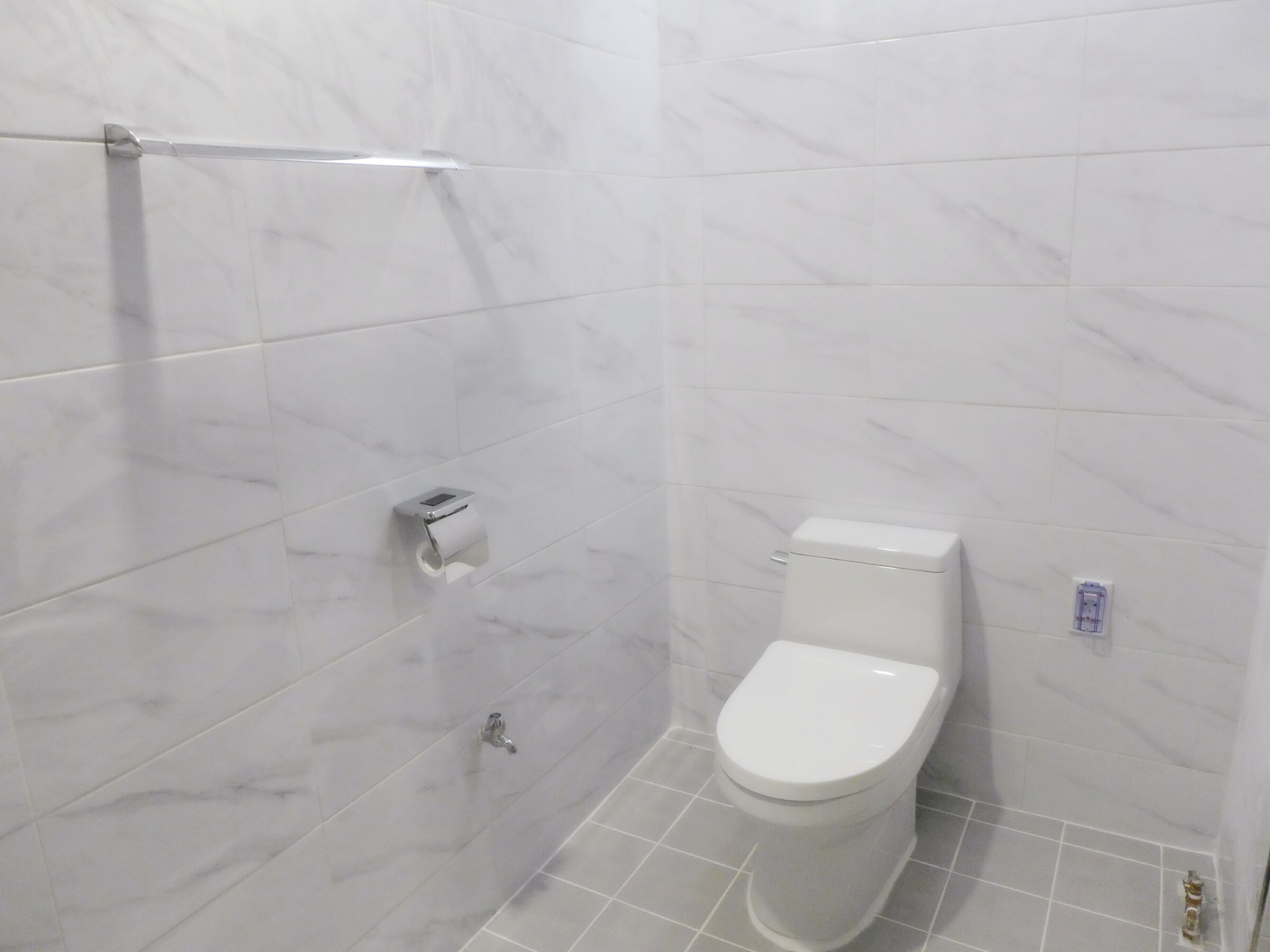A bathroom with a toilet, a paper towel dispenser, and a shower area.