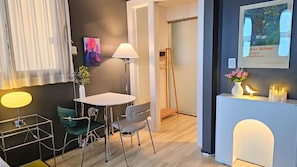 Ein modernes Hotelzimmer mit Essbereich, Stehlampe, Gemälde, Rezeption und einer Vase mit Blumen.