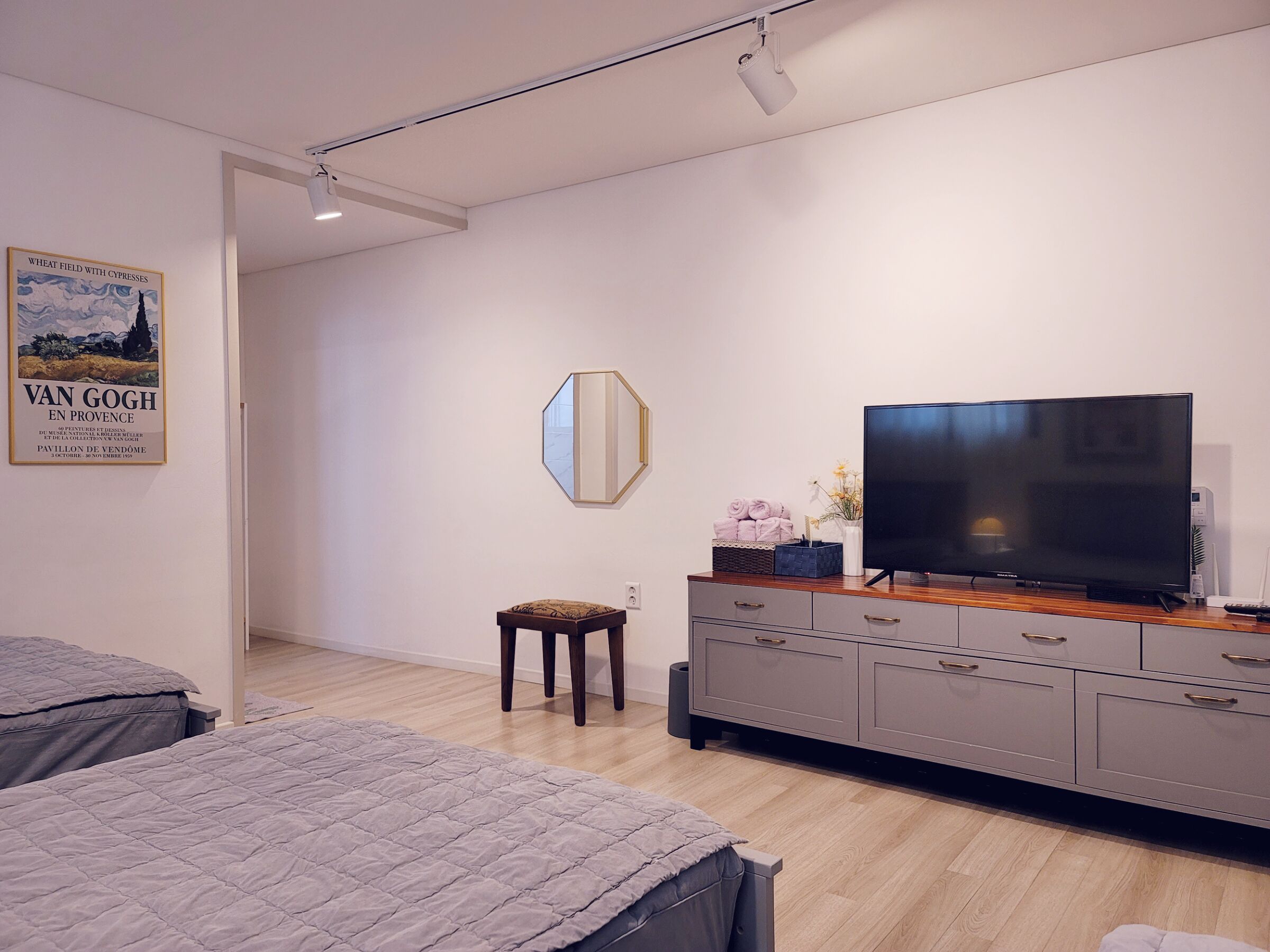 Ein modernes Schlafzimmer mit einem großen Flachbildfernseher, einer Holzkommode und einem kleinen Hocker.