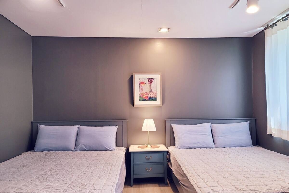A modern bedroom with two beds, a nightstand, a lamp, and a framed picture on the wall.