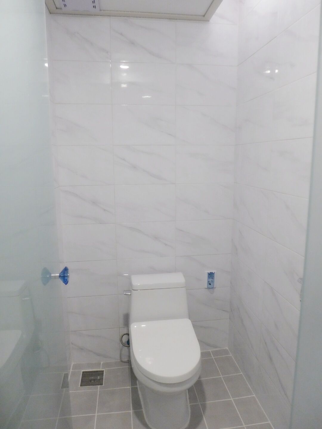 Un baño pequeño con azulejos blancos, que incluye un inodoro, una ducha y un desagüe.