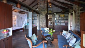 Ein rustikales Zimmer mit Steinwand, Holzbalken an der Decke, einem Himmelbett, einem blauen Sofa und einem Bücherregal voller Bücher.