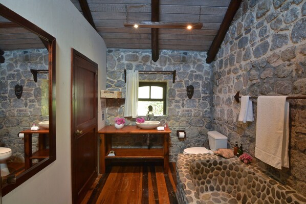 A rustic bathroom with stone walls, a wooden vanity, a stone bathtub, and a wooden door.