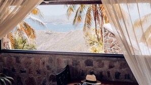Ein Zimmer mit Stehwänden, einer Bank mit Hut und Sonnenbrille und Blick auf Palmen und Strand.