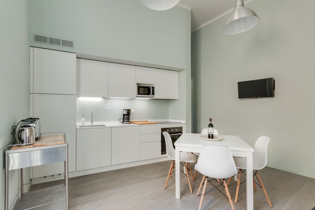 Une cuisine moderne avec des meubles blancs, un four à micro-ondes, un évier, une machine à café et une table à manger avec des chaises.