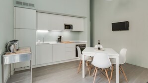 Eine moderne Küche mit weißen Schränken, einer Mikrowelle, einem Spülbecken, einer Kaffeemaschine und einem Esstisch mit Stühlen.