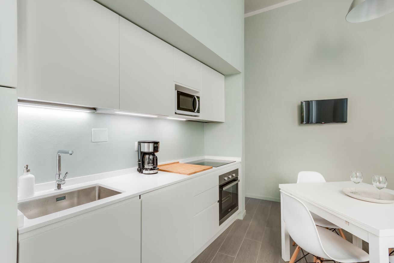 A modern kitchen with white cabinetry, a microwave, a coffee maker, and a dining area with a white table and chairs.