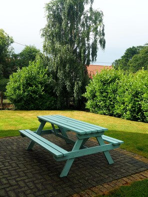 Ein Picknicktisch in einem Garten mit einem Pflasterweg und üppiger Bepflanzung.