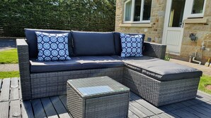 Ein Korbsessel mit Kissen und ein passendes Ottomanen auf einer Holzterrasse.